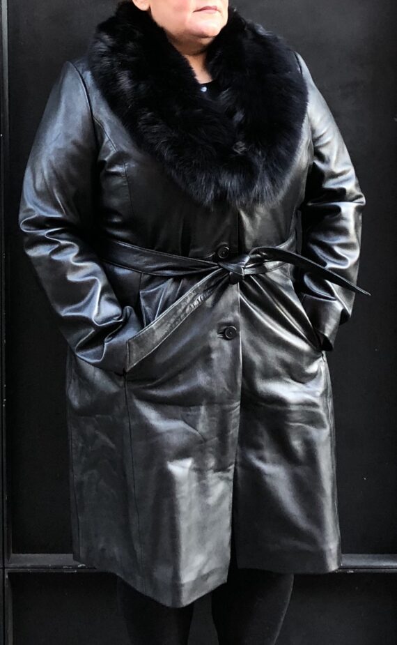 A woman wearing a black lambskin coat with a fox fur collar and a black hat.