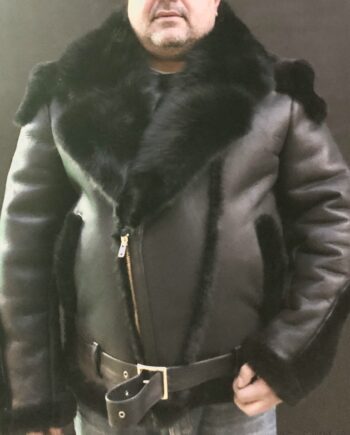 A black sheepskin biker jacket with a detachable fox fur collar, standing in front of a gray wall. The jacket has a zip front closure, two side pockets, and a belt at the waist.