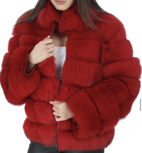 A woman wearing a red fox fur jacket with a hook and eye closure and two side pockets, looking luxurious and glamorous.