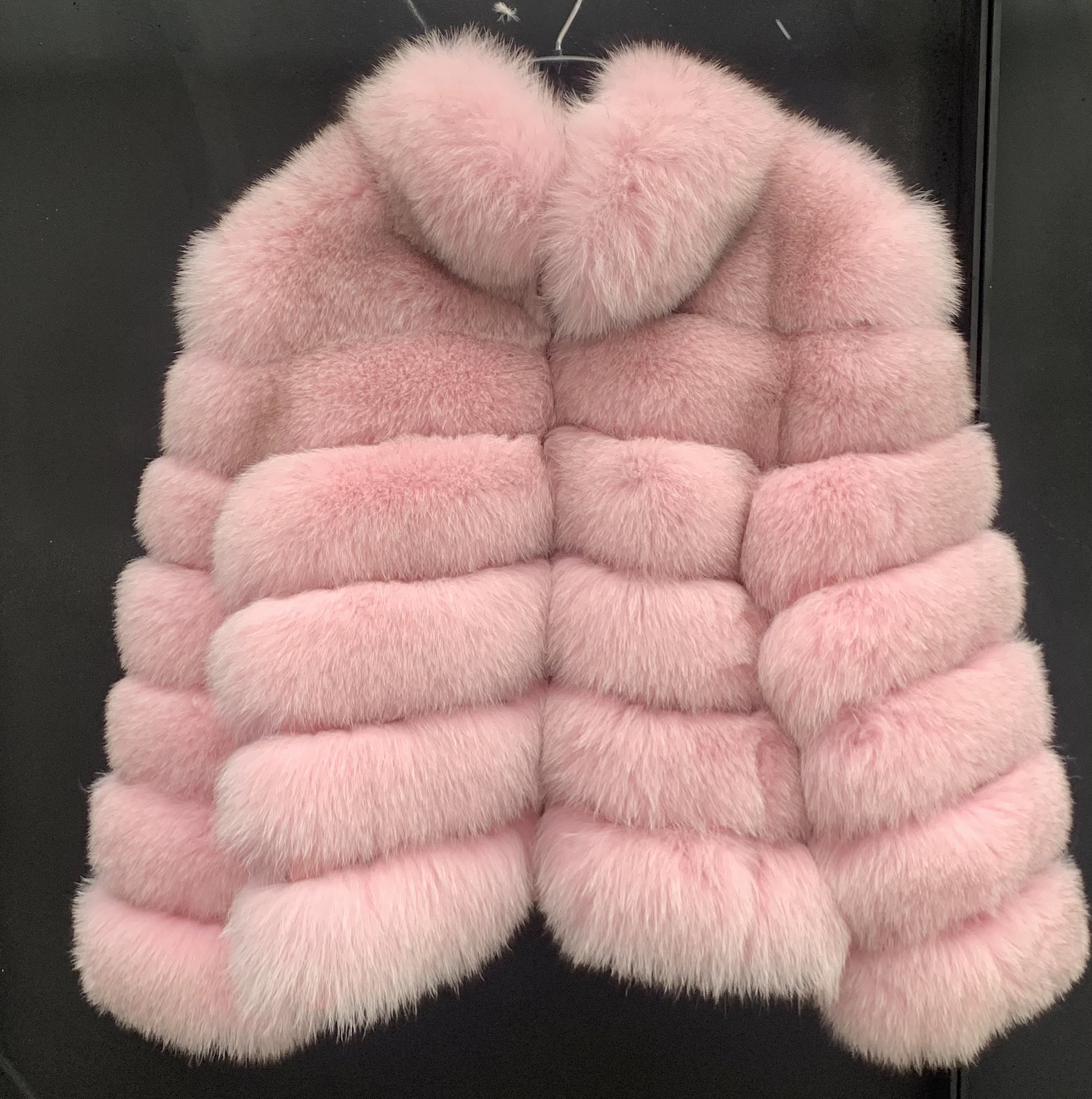 A woman wearing a pink fox fur jacket with a zipper and pockets.